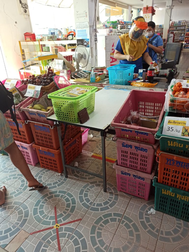 Different measures done by local super market to prevent virus spreading: they marked, where we can stand; they put one extra table beetwen shopper and cashier; you have to put product from your basket to the blue basket and you give money or card in the fish sack net. The only problem is that in most of the Thailand don't have contactless card  payment option, so when you gave the cashier a card, you have to go around next to her and put a pin. But they put a sanitizer gel next to the card machine and you must use it before writing a pin.